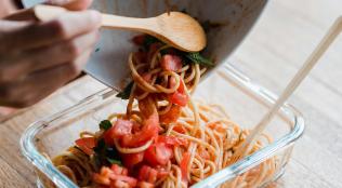 Pasta being scraped into a glass food container
