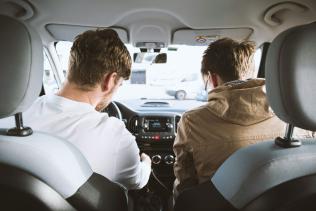 Two men driving a car viewed from the backseat.