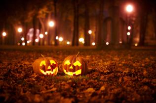 Two pumpkins sit lit up in a dark park.