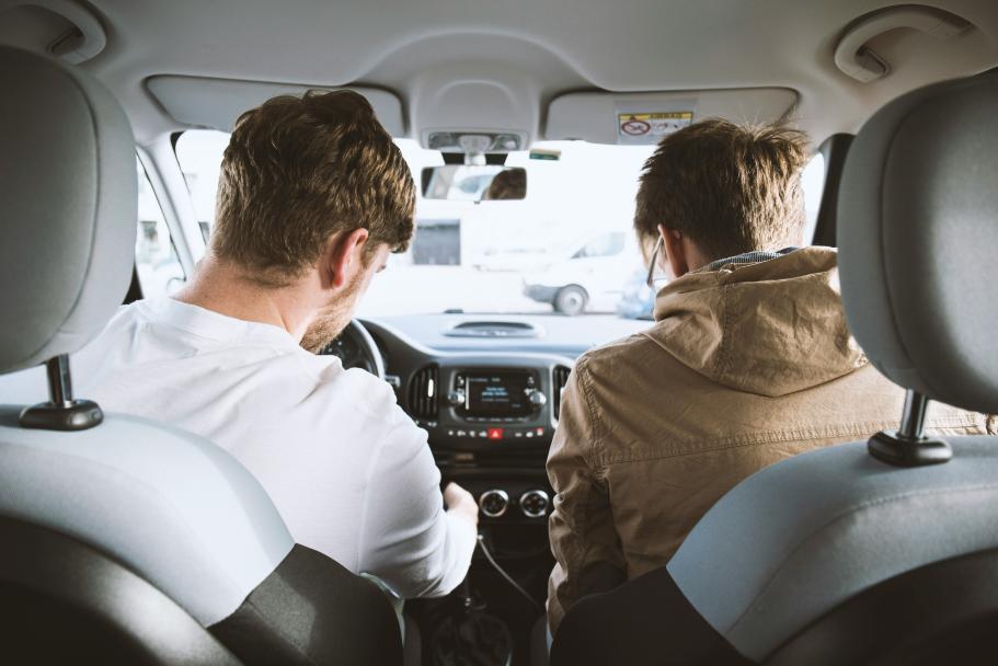 Two men driving a car viewed from the backseat.