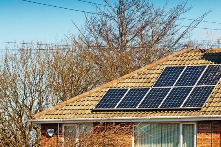 Solar panels on a brick home with a blue sky and trees in the background.