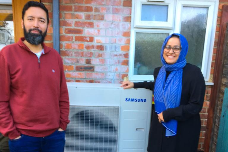 Two people smiling on either side of a heat pump