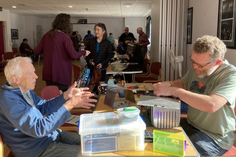 Two mean talking to one another across a table of repaired goods