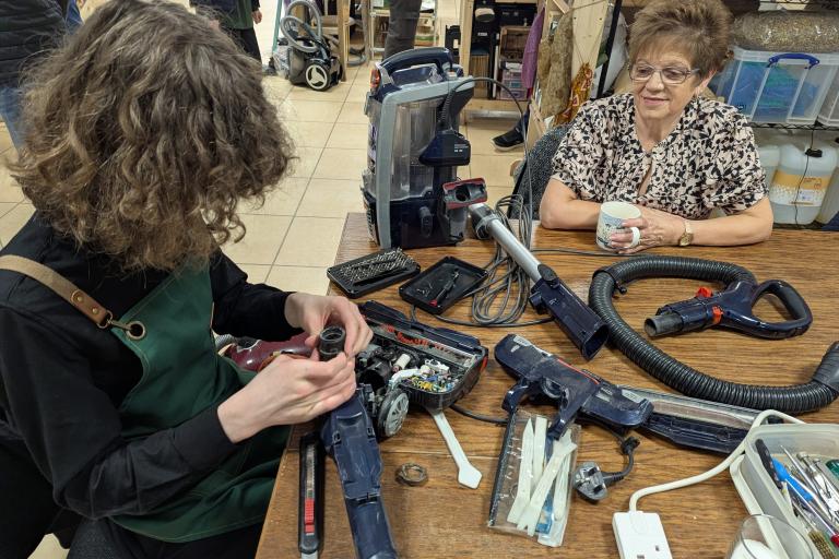 Two women repairing a hoover at a table