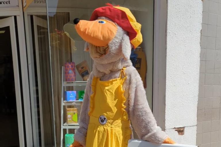 A person in a yellow womble suit standing by a sign for the repair cafe