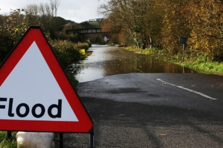 Flood sign next to a road with water flooded on it