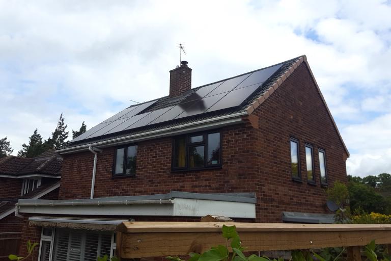 The upper-half of a red brick house displays its solar panels on its slanted roof.