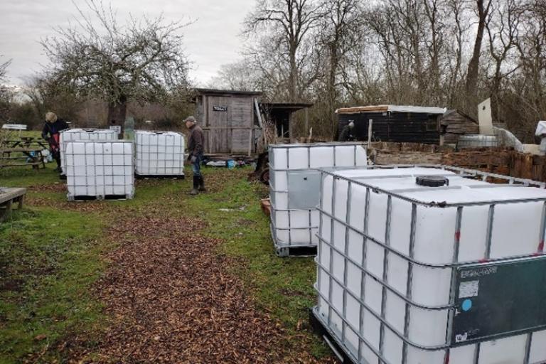 Five 1000l IBC tanks are dotted around an open patch of the garden on a cloudy day, ready to be moved-in and installed.