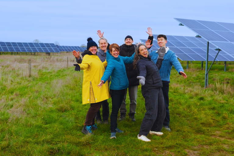 Low Carbon Hub colleagues smiling at the camera, proudly showing off a series of solar panels in the field behind them