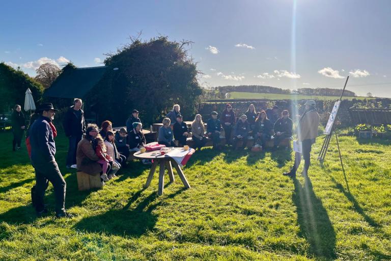 A large group of people gather on some grass on a sunny day.