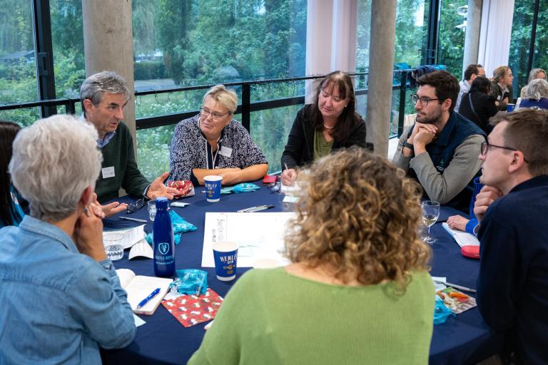 A group of people gather around a table, sitting down, having a discussion.