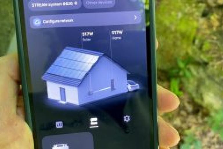 A hand holds up a smartphone which is displaying an app that shows the amount of energy generated by the solar panels.