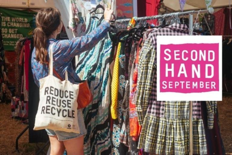 A woman browses some clothes racks in Oxfam, holding a tote bag displaying the slogan 'reduce, reuse, recycle'.