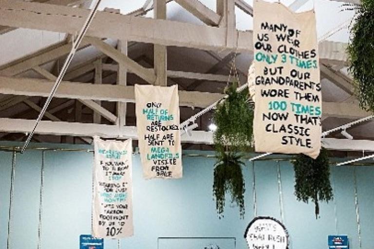 Banners hang from a ceiling displaying different facts about the fashion industry's impact on the planet.