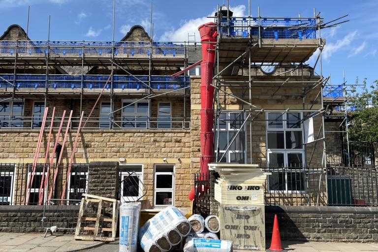 Scaffolding surrounding a brick house, with insulation packaged up outside.