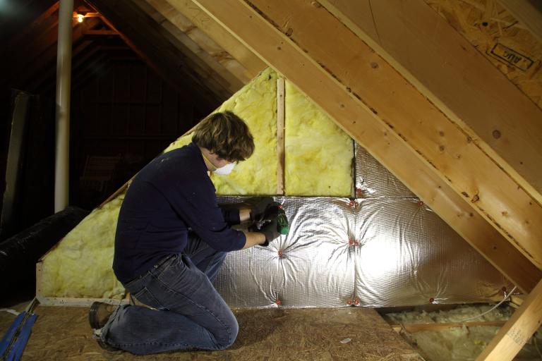 A person wearing a face mask installing insulation in an attic.